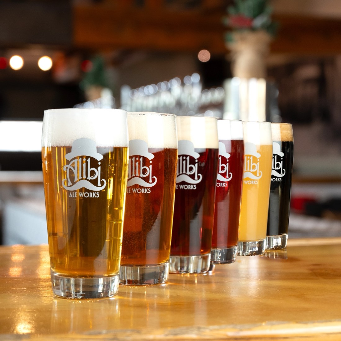 A lineup of Alibi Ale Works beers in branded pint glasses